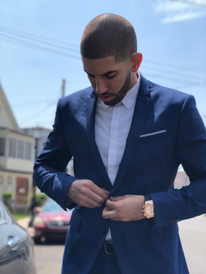 Contact A fashionable man in a blue suit adjusting his jacket button outdoors in Stratford, CT.